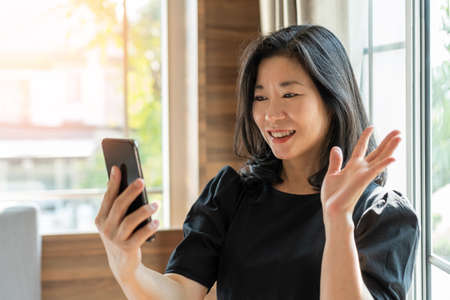 Video call on zoom meeting at home in new normal lifestyle for social distancing during lock down with woman user waves hand greeting on mobile smartphone call using social media appの写真素材