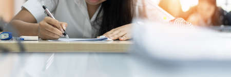 Exam at school with student's taking educational admission test in class, thinking hard, writing answer in university classroom, education and world literacy day conceptの写真素材