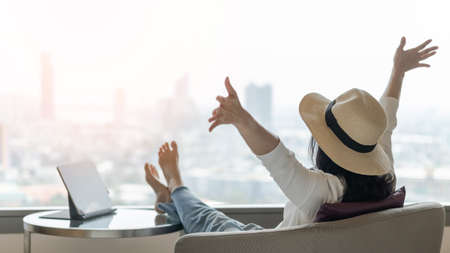 Work-life balance, summer holiday vacation concept with happy woman taking a break, celebrating successful work done, casually resting in luxury home or city hotel workplace with computer laptop on deskの写真素材