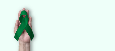 Emerald Green (Jade) ribbon awareness color for Liver Cancer and Hepatitis B - HVB month (bow isolated on background on hand)の写真素材