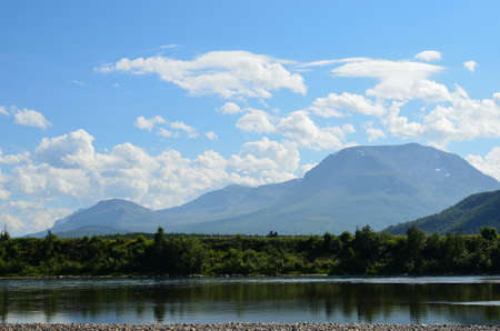 Landscape photo of the Maalselv river with the mountain of Alapen surrounded by hovering clouds on a vivid blue sky backdropの写真素材