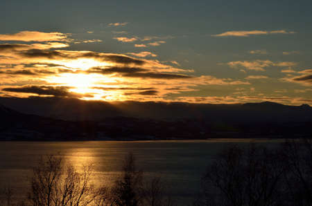 sun behinds clouds with fjord in foreground