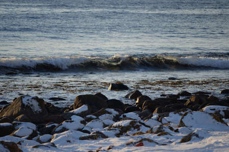 waves washing in over snow covered rocks on the sea shoreの写真素材