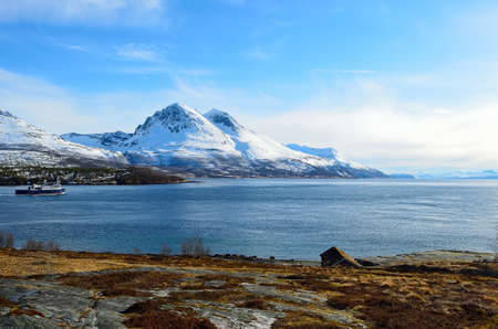 Majestic snow covered mountain with a blue sky and ocean in front with slow moving boat in Hella, Norway in spring timeのeditorial素材