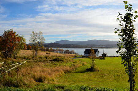 blue autumn sky, green field, house and fjordのeditorial素材