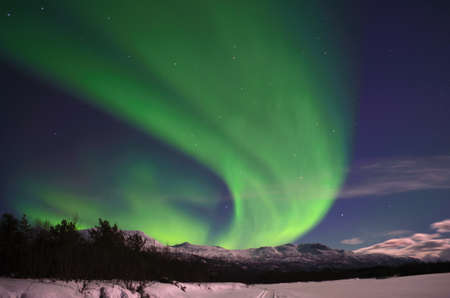 Aurora borealis on arctic winter night over snowy mountain on a frozen snowy river bedの写真素材