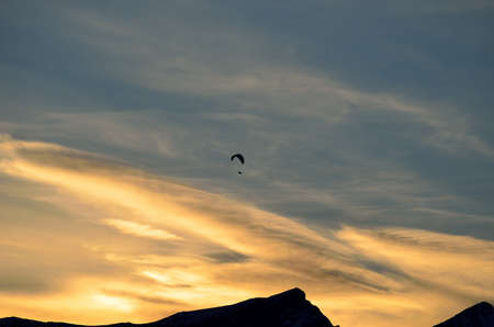 Paraglider on vibrant colourful dawn sky with majestic snow covered mountain underneathの写真素材
