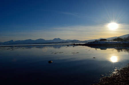 sunshine over silent fjord with vibrant blue sky and majestic mountain range in the far distance