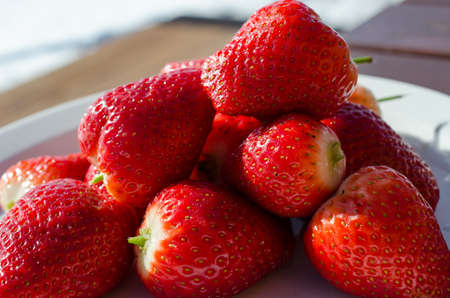 red vibrant strawberries on white platter outside in easter sunの写真素材