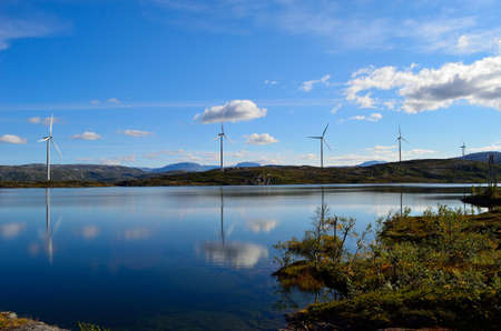 windmill farm on mountain top reflecting in the lake water on sunny blue autumn dayの写真素材