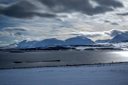 Deep snowy mountain landscape on sunny day with blue fjord
