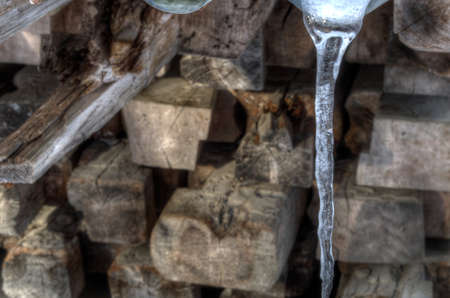 Melting icicle hanging in front of wooden pole stackの写真素材