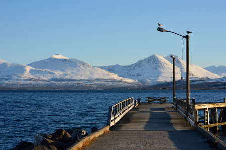 long pier in blue fjord with snowy mountain range in backgroundの写真素材