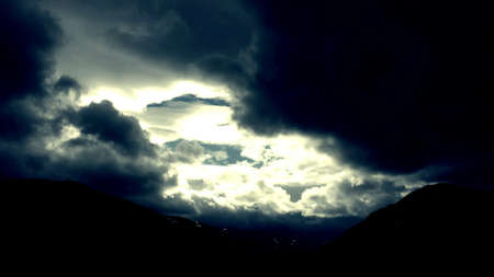 Dark clouds over mountains with small patches of blue sky and sunshineの素材
