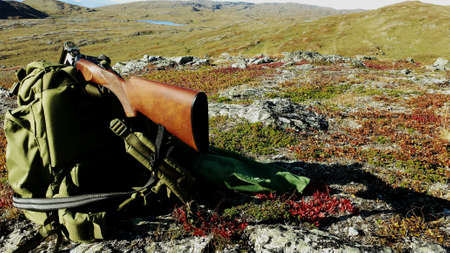 Shotgun on green backpack and grouse bird in hunting net with mountain landscape backdrop in autumnの素材