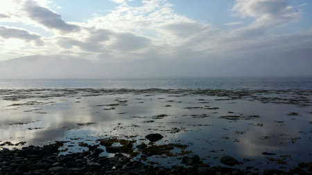 Thick white sea fog shrouding mountain range on a blue autumn day with blue sky reflection on fjordの素材