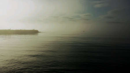 Stone pier into blue fjord with thick sea fog blowing over ocean surfaceの素材