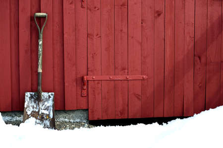 old snow showel resting on red barn wall in snowy winterの写真素材