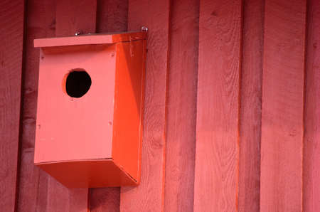 red bird house on barn wall in sunshineの写真素材