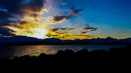 Golden sunny sunset over snowy mountain range with reflection on sea surfaceの素材