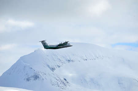TROMSOE, NORWAY - APRIL 17, 2015: Wideroe propeller airplane climbing on sky after takeoff from...