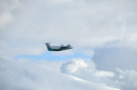 TROMSOE, NORWAY - APRIL 17, 2015: Wideroe propeller airplane climbing on sky after takeoff from...