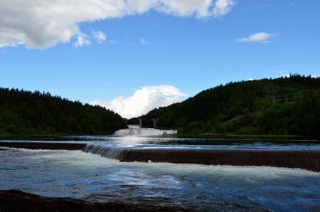 beautiful summer landscape with waterfall, river flow and hydro electrical plate water gates in the backgroundの写真素材