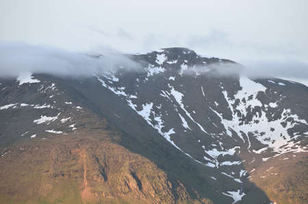 mighty mountain peak with clouds and snow patches in summerの写真素材