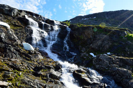 majestic waterfall on summer mountain in the arctic circle with snow patchesの写真素材