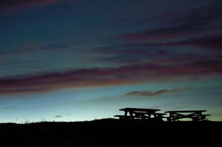 beautiful wooden park bench silouhettes with dawn sky backgroundの写真素材