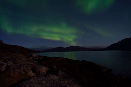 mighty aurora borealis dancing on night sky over mountain and fjord landscape in late autumn in the arctic circleの写真素材