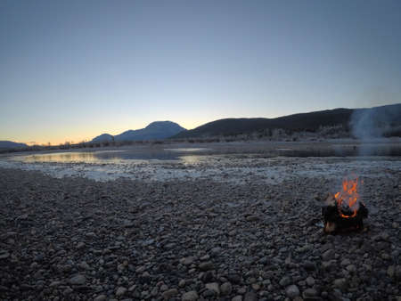 warming fire on frozen cold white river shoreの写真素材