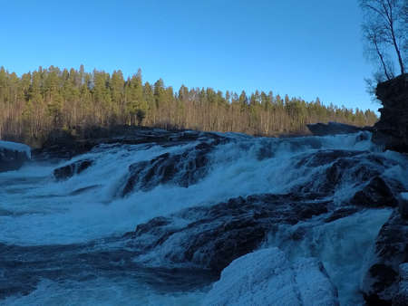 mighty frosty waterfall in late autumn with forest backgroundの写真素材