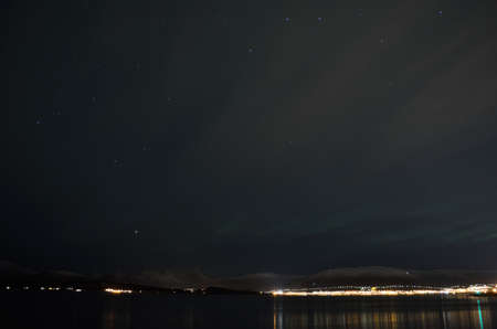 aurora borealis over snowy mountain and calm fjord in autumn night