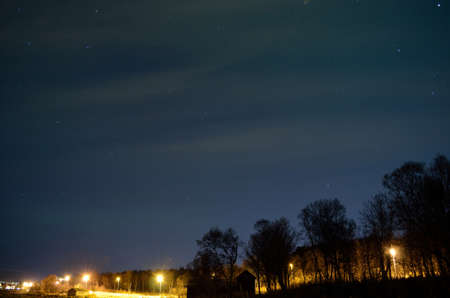 aurora borealis over lit public road, forest and buildingsの写真素材