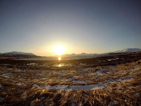 long brown grassy field with golden sunrise over mountain and fjordの写真素材