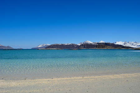 majestic white springtime beach with snowy mountain islands in sea on the summer island in northern norwayの写真素材