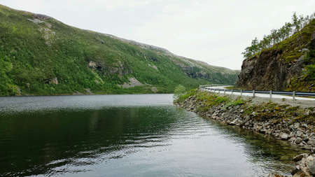 Calm mountain fishing lake background with road on the right sideの素材