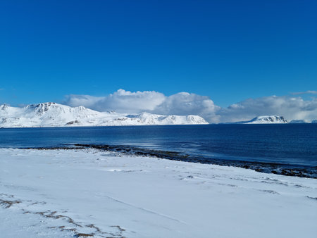 sunny blue sky and sea with white snowy mountains on the island of mageroya in north cape countyの写真素材