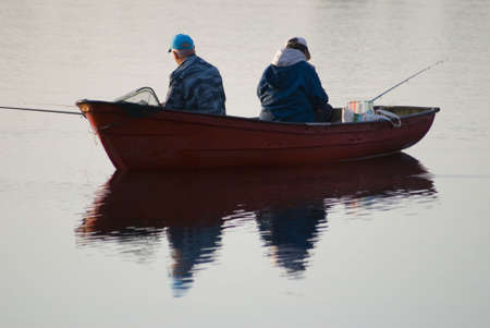 Two persons sit in a boat and fishの写真素材