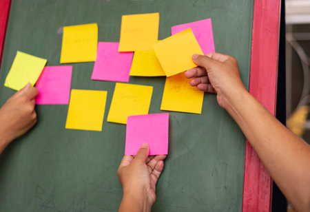 Hands of teacher and student writing on sticky notes on blackboardの写真素材