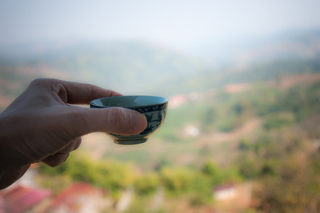 Glass teapot with hot green tea and cup of tea  and Mountain view background (Blurred Background)