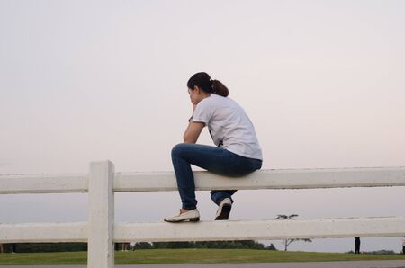 woman wore a white t-shirt and jeans sitting on a white fence.の写真素材