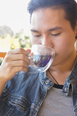 Young man smiling face. young man holding coffee cup or hot tea while sitting at his coffee shop with a natural view.の写真素材