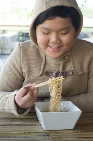 Eating noodles at restaurant. winter day Young Asian boy eating ramen noodles using chopsticks .