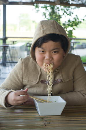Eating noodles at restaurant. winter day Young Asian boy eating ramen noodles using chopsticks .の写真素材
