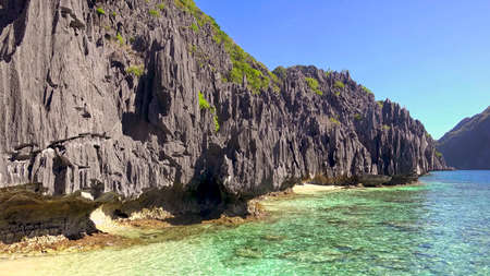 Gorgeous view of the beach with clear water, blue sky and green mountain with big rocksの写真素材