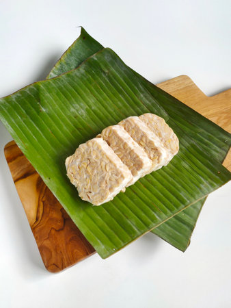 Cut tempeh on banana leaves and wooden cutting board. Tempeh is one of vegetable protein source and...