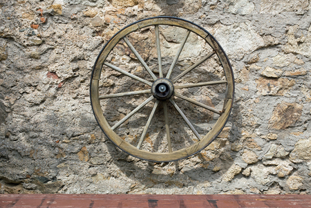 Old wooden wagon wheel on a stone wallの写真素材