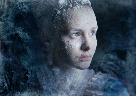 Beautiful young girl looking through a frosty windowの写真素材